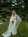 Bride in a white veil and gown holding a bouquet, standing on a garden walkway.