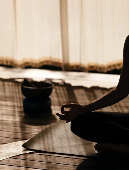 Person sitting cross-legged on a yoga mat practicing meditation with hand in mudra gesture indoors.