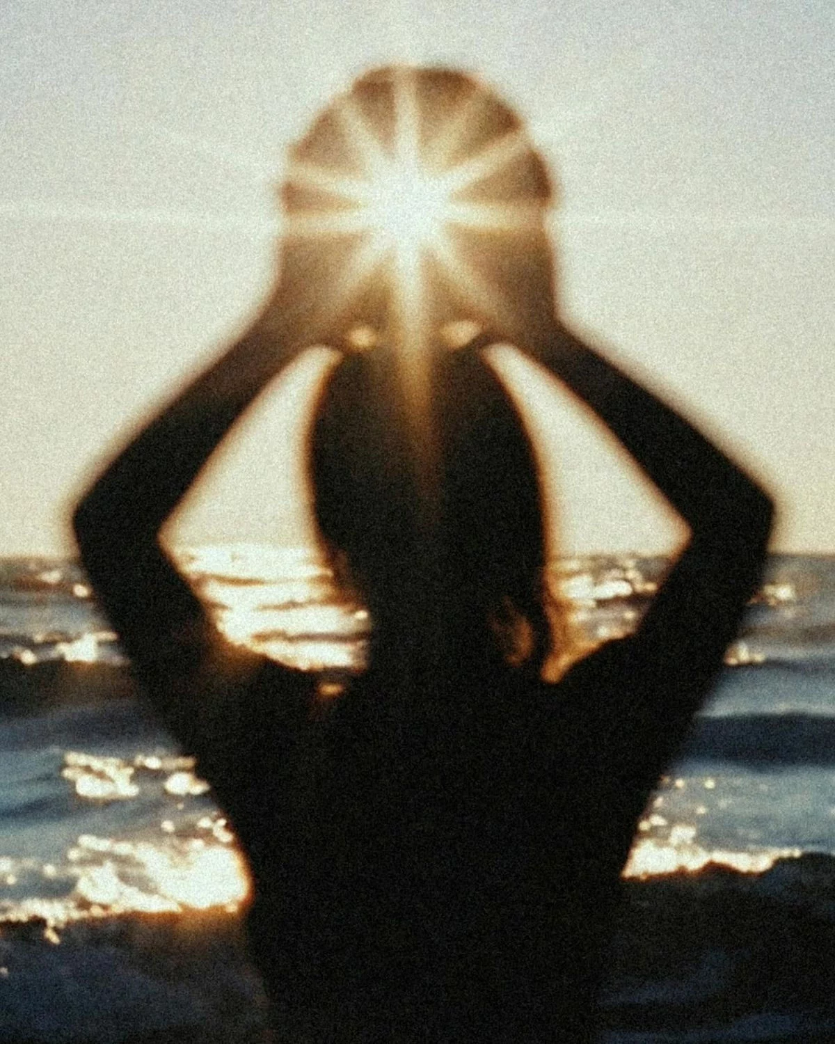 Silhouette of person holding sun with hands shining brightly over the ocean at sunset.