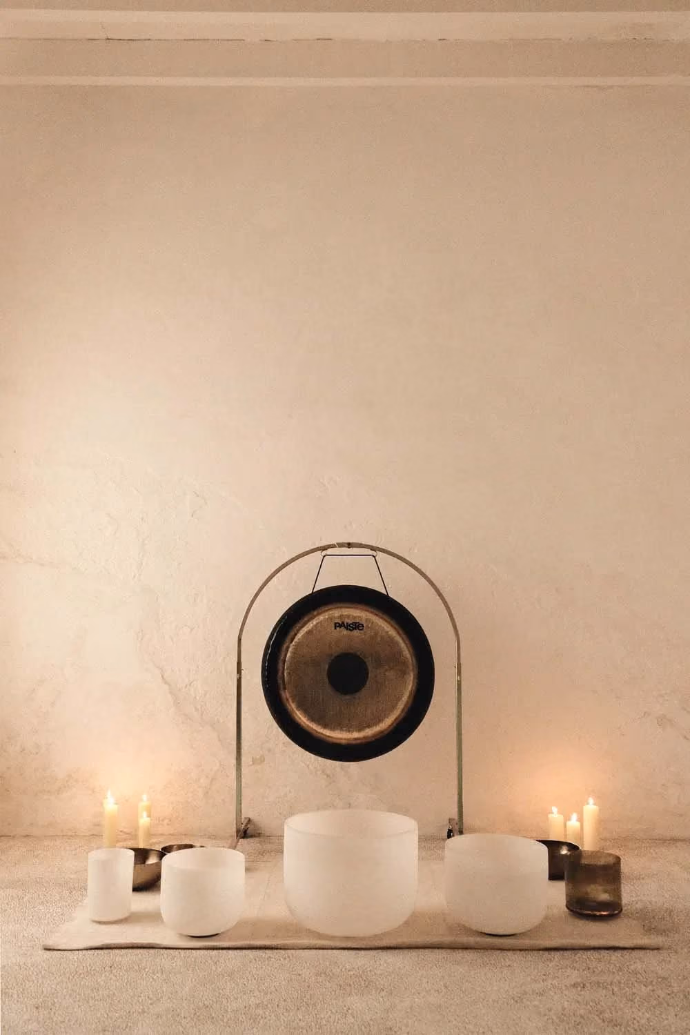 Gong, crystal singing bowls, and lit candles arranged for a sound healing session.