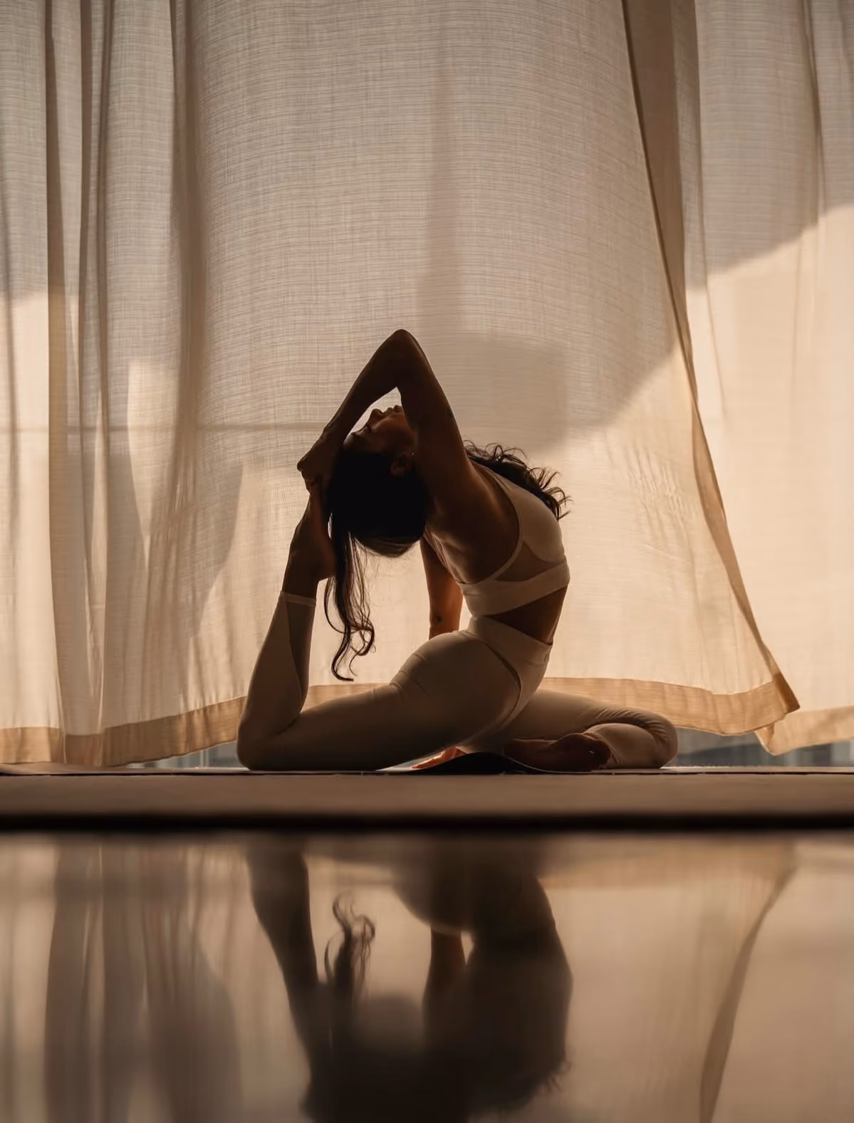 Silhouette of a woman in a yoga pose with backbend stretching her foot behind her head.