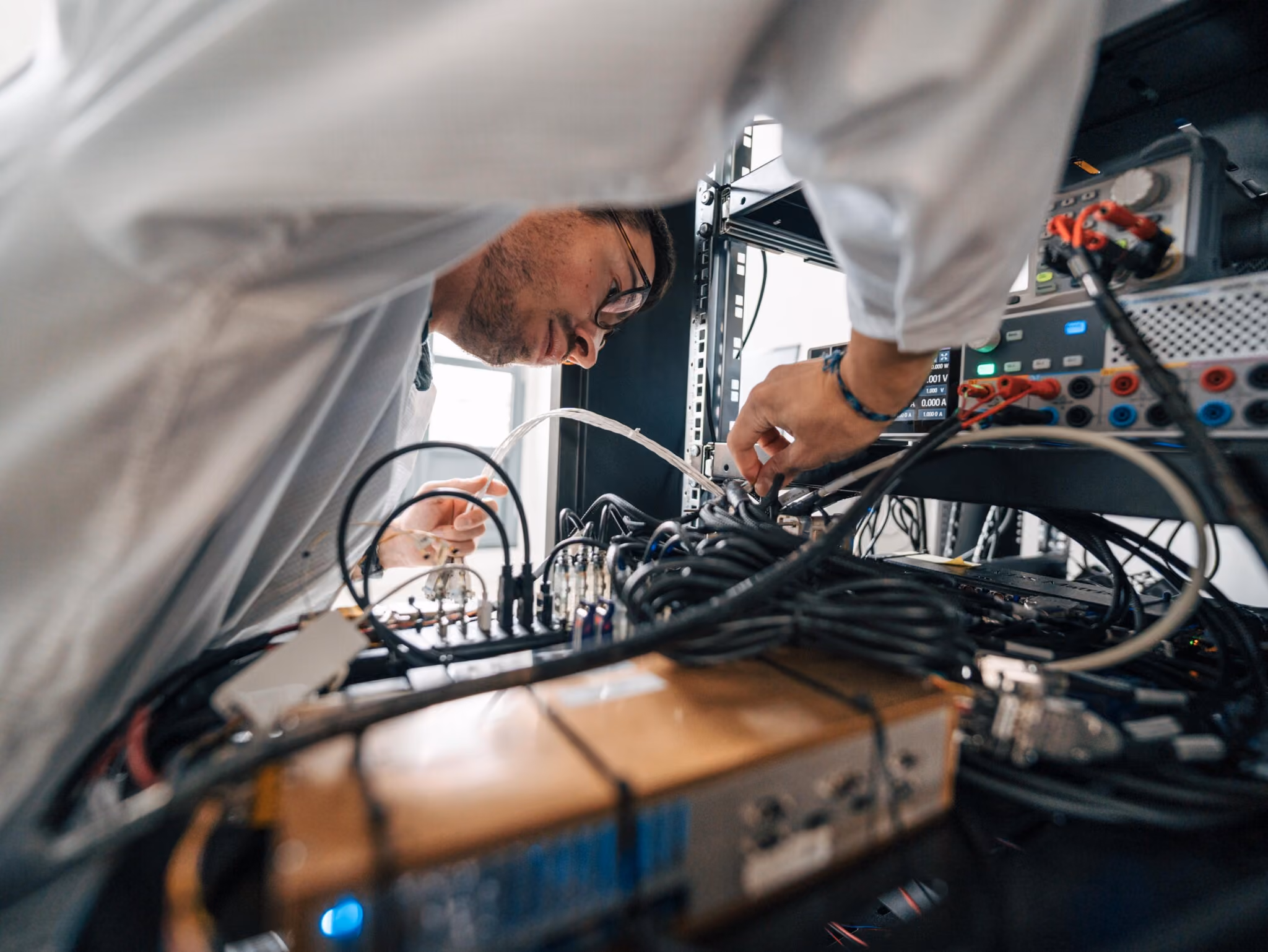Man in lab coat working on electronic equipment with wires and testing devices.