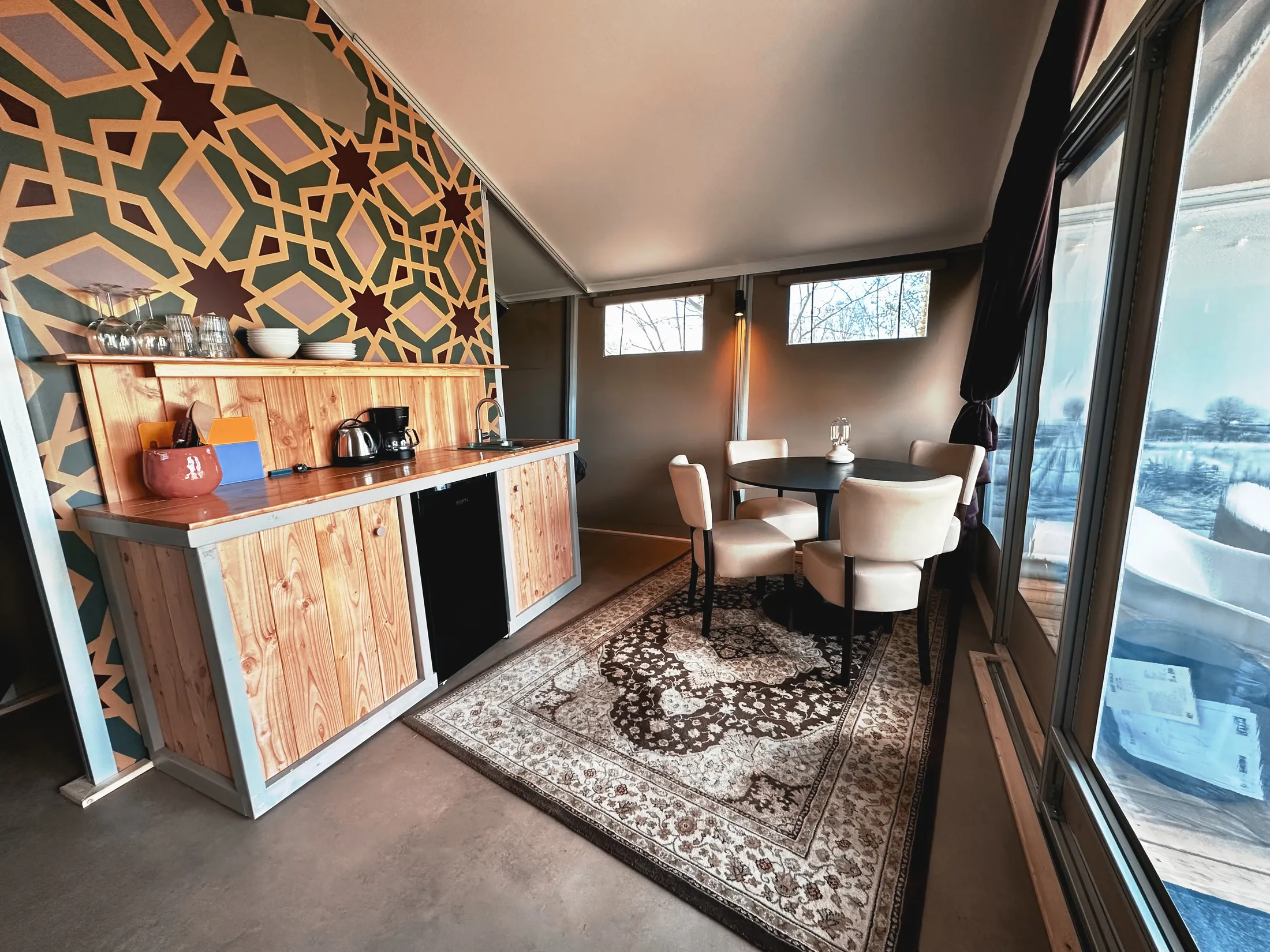 Moderne keuken en eetruimte met houten kast, rond tafel, vier stoelen en groot raam met uitzicht.