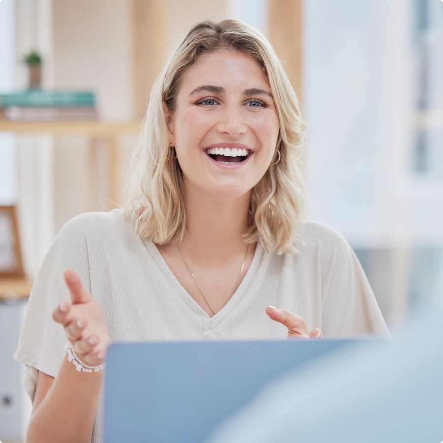 Smiling blonde woman wearing a light beige top and gold hoop earrings talking animatedly in a bright indoor setting.
