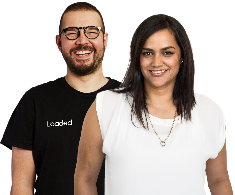 Smiling man with glasses wearing a black Loaded T-shirt standing behind a smiling woman in a white blouse and gold necklace.
