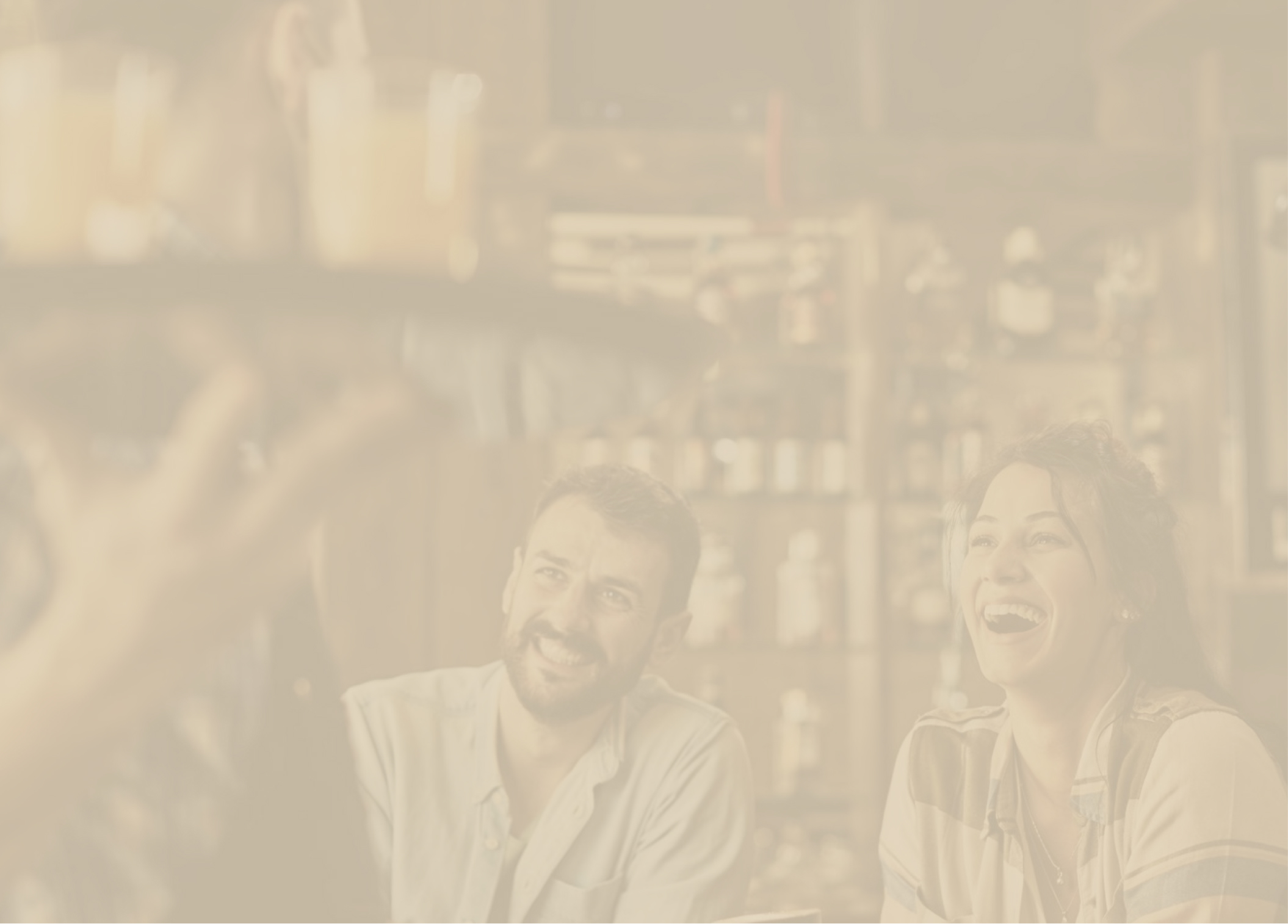 A man and woman smiling and laughing while engaged in a conversation in a cozy cafe setting.