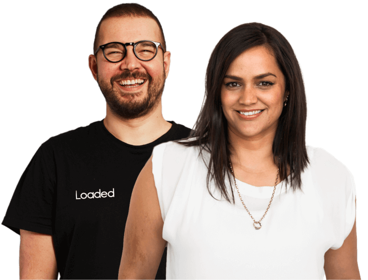Smiling man wearing glasses and a black Loaded t-shirt stands behind a smiling woman in a white top with a necklace.