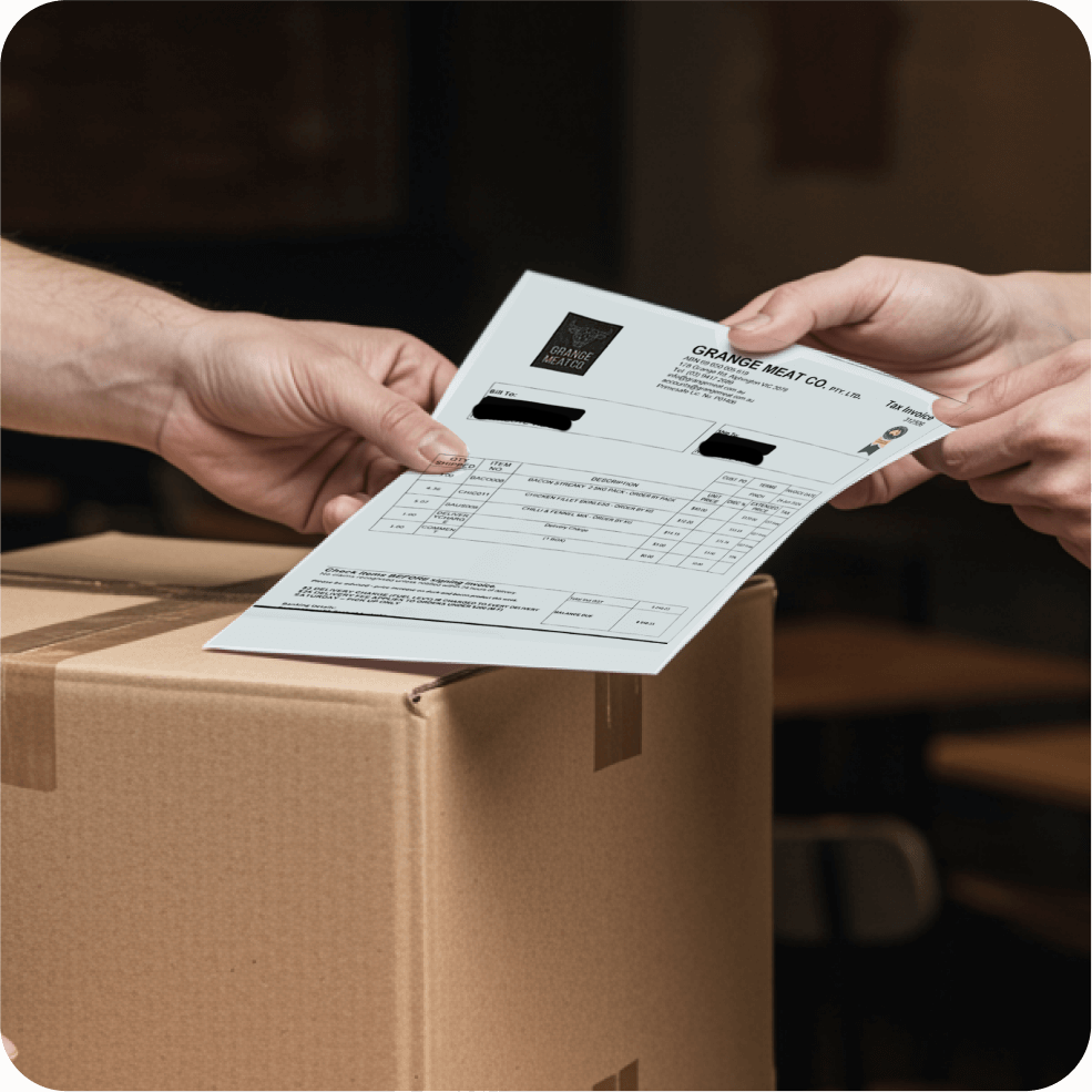 Two hands exchanging an invoice document over a cardboard box in a dimly lit setting.