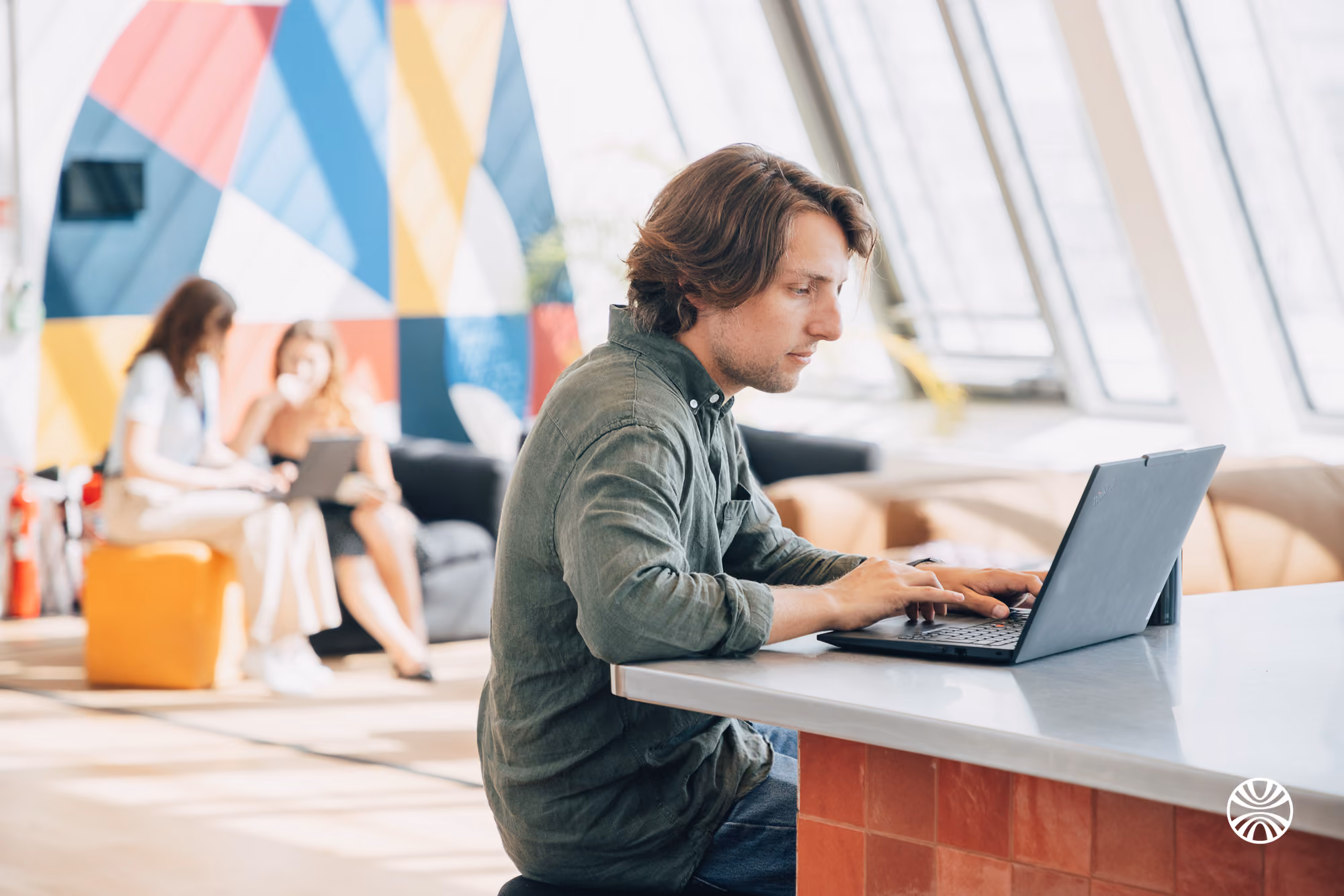 Man in green shirt working on a laptop at a white counter in a bright, colorful office space.