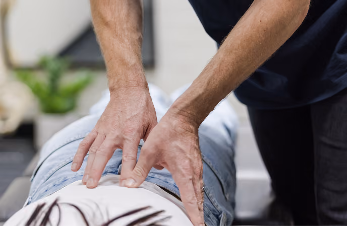Hands of a chiropractor pressing on a patient's lower back during a treatment session.