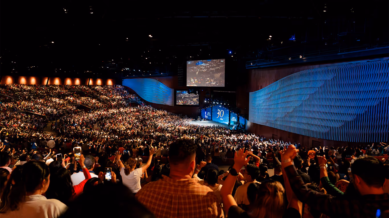 Gran multitud en auditorio con escenario iluminado y pantalla que muestra 30 años de evento.