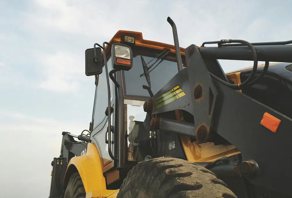 Close-up of a yellow and black farm loader tractor with large front tire and cabin visible.