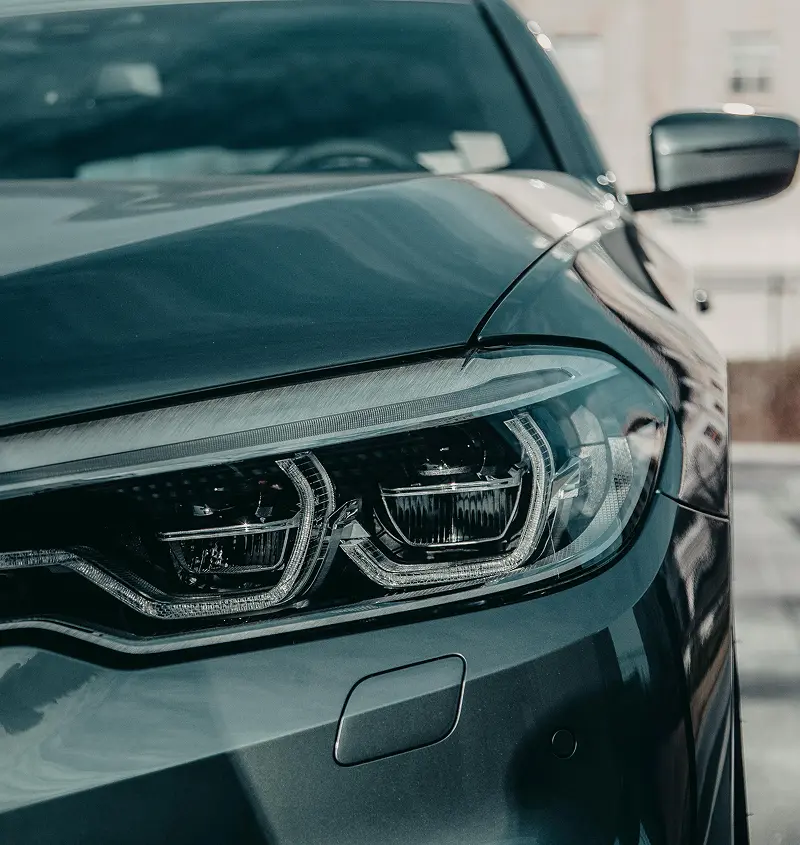 Close-up view of a dark-colored car's front left headlight and side mirror.