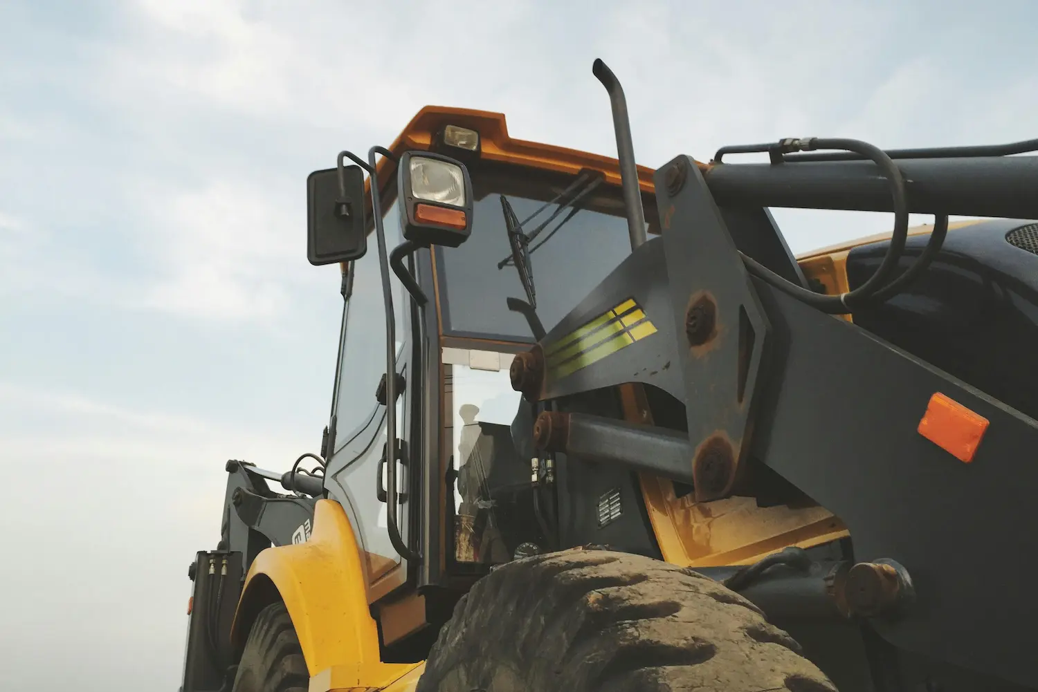 Close-up of a yellow and black heavy construction vehicle with large tires against a cloudy sky.