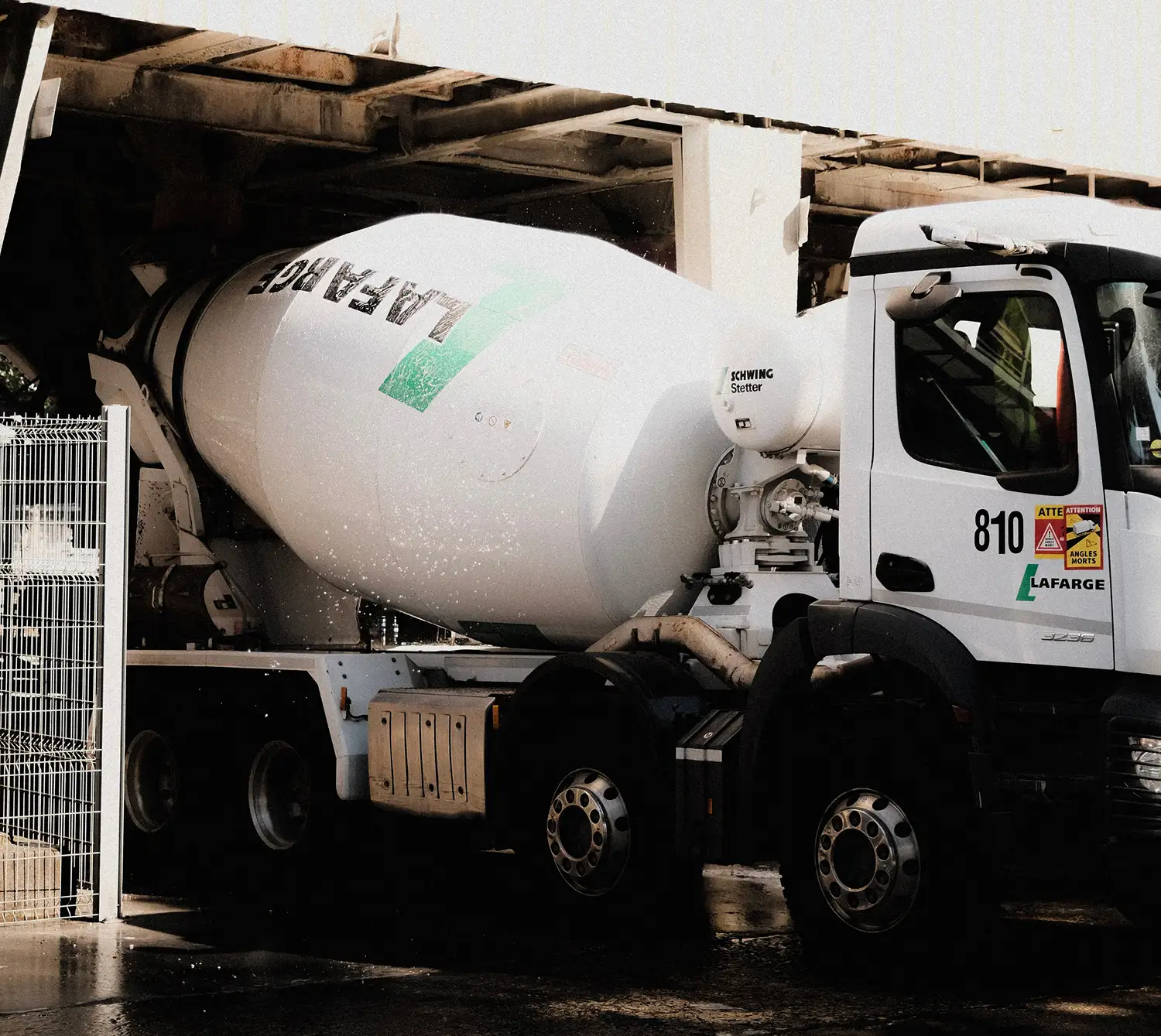 White Lafarge cement mixer truck parked under a structure with water splashing around its drum.