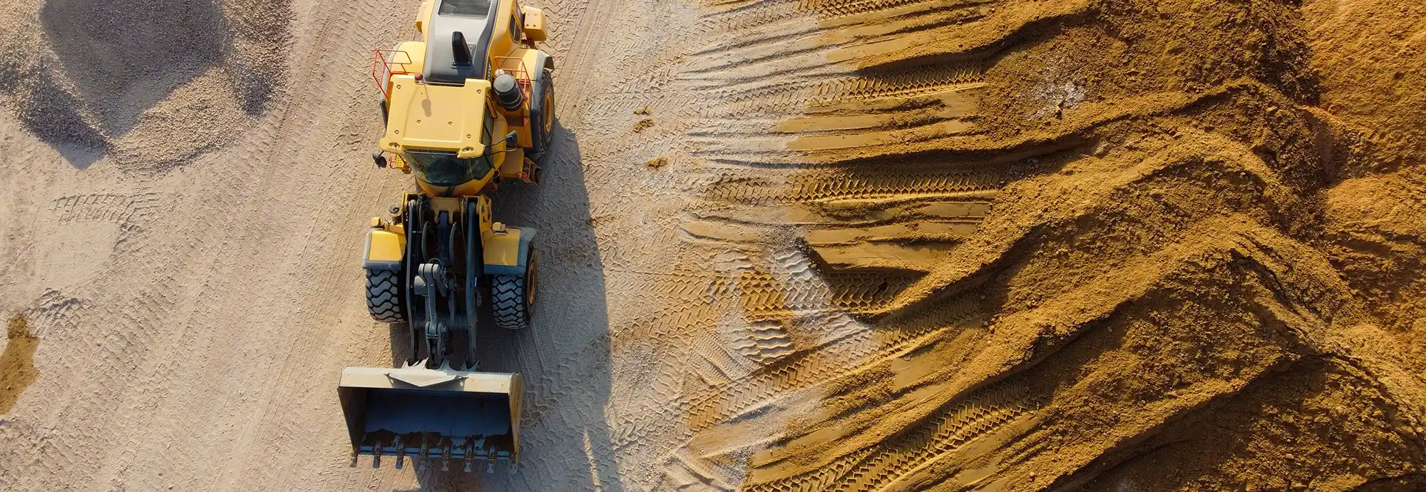 A yellow earthmover with a front loader is parked on a dirt site with tire tracks.