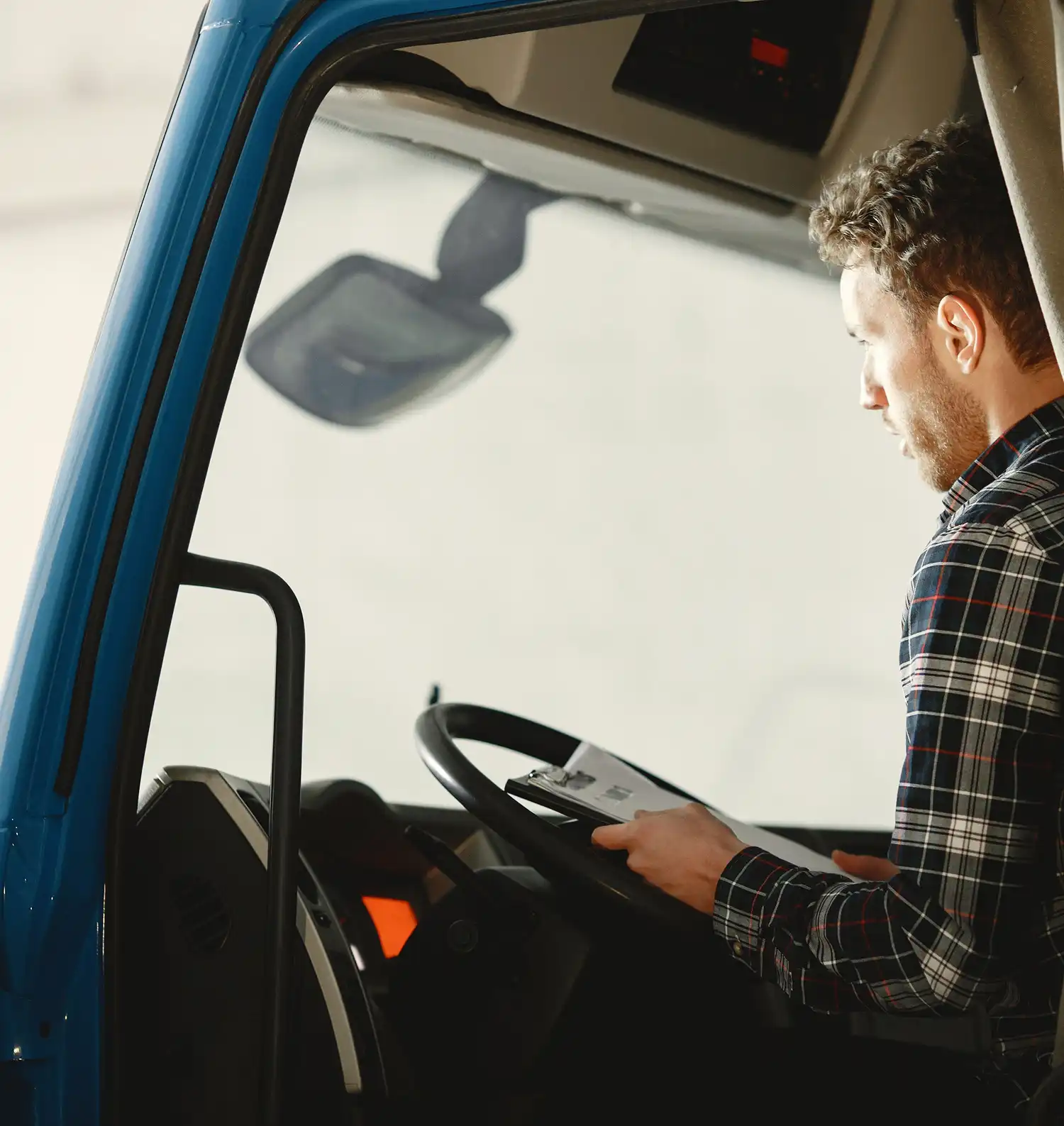 Man in plaid shirt sitting in a blue truck cab reading papers on a clipboard.