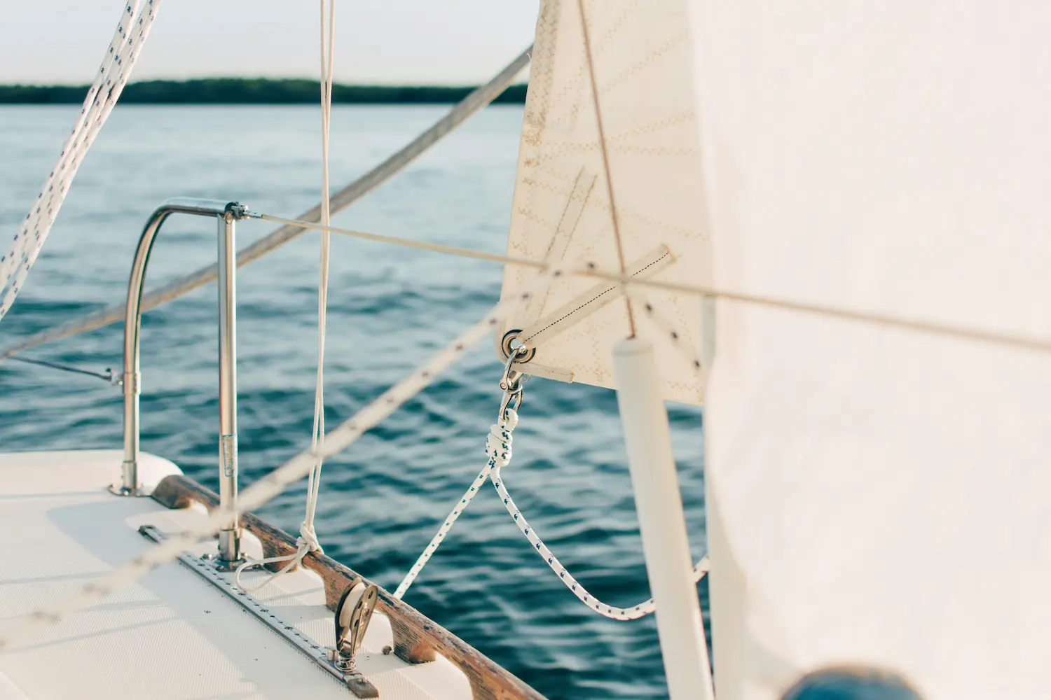 Close-up of sailboat rigging and ropes with calm water and distant shoreline in the background.