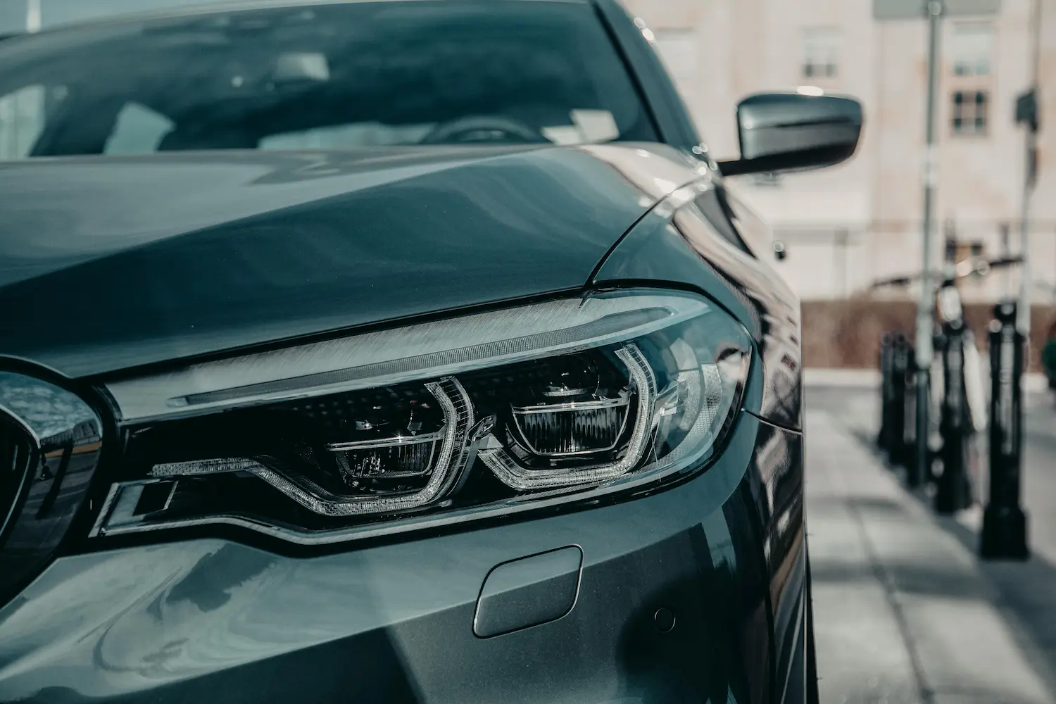 Close-up of a modern car's headlight and front side mirror on a city street.