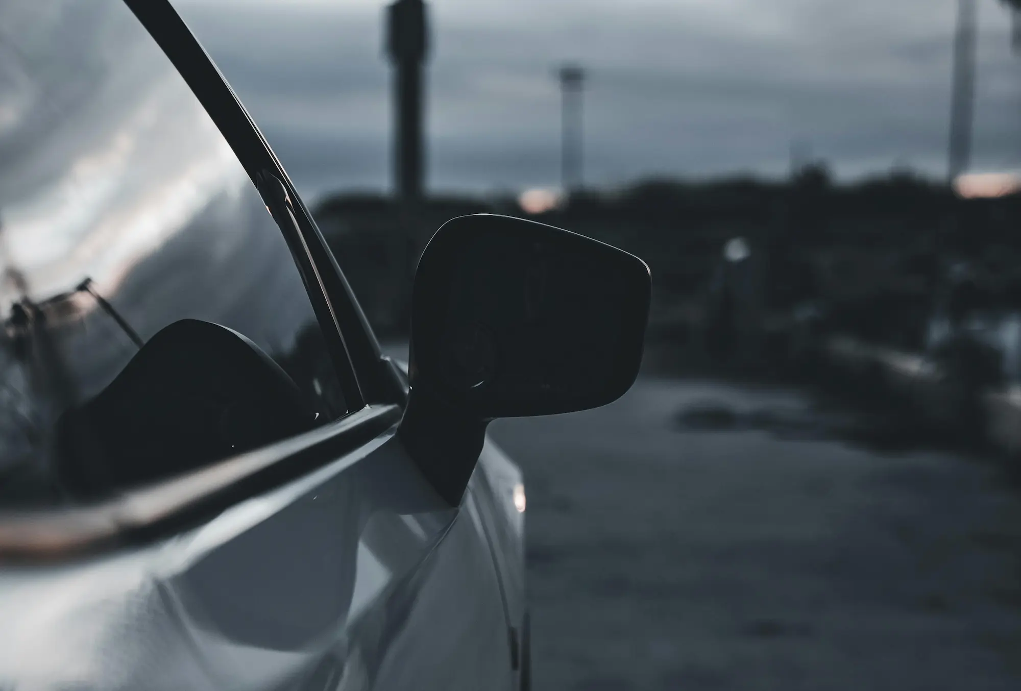 Close-up of a car's side mirror at dusk with a blurred background.