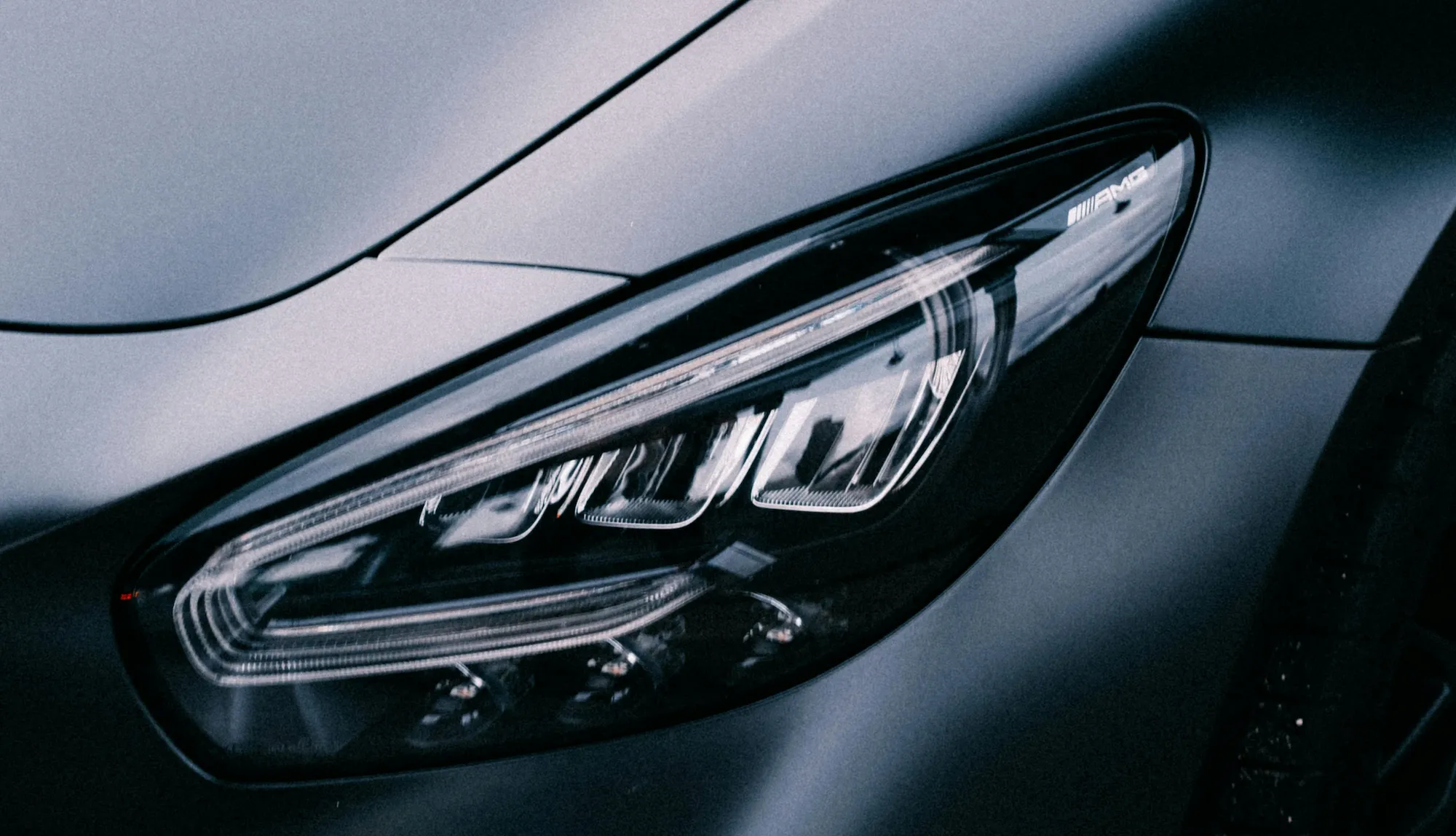 Close-up of a sleek car headlight with AMG branding on the dark gray body panel.