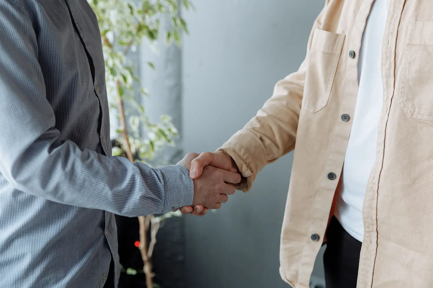 Two people shaking hands; one in a plaid shirt, the other in dark workwear holding a tool.
