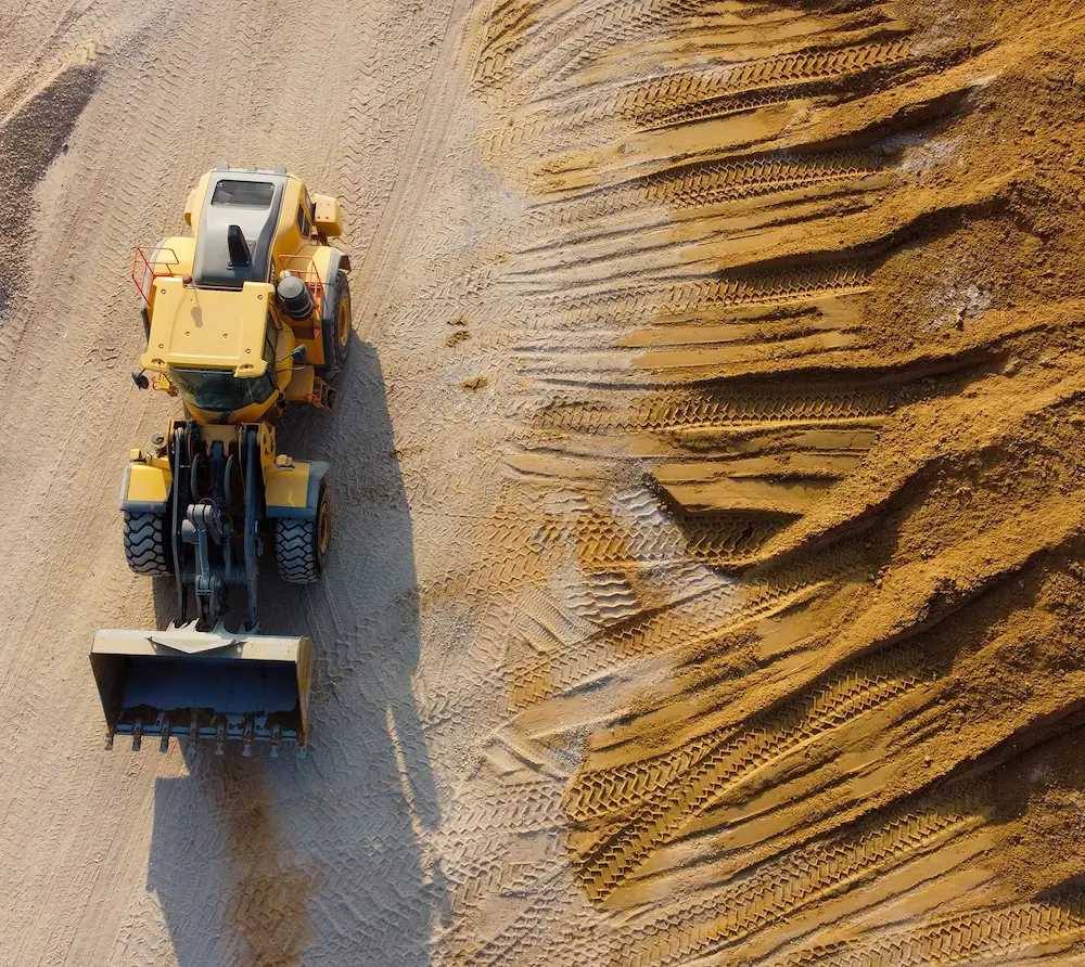 A yellow earthmover with large tires parked on dirt with deep tire tracks on the ground.