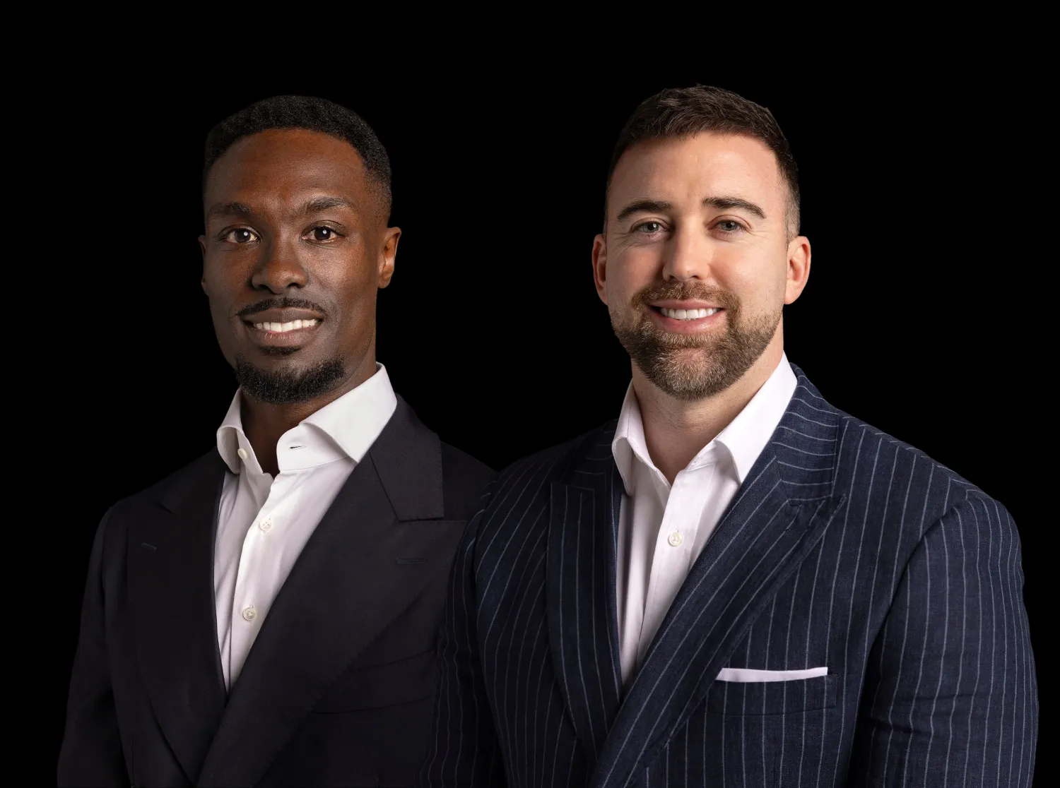 Two men in business suits smiling, one in pinstriped navy, other in solid black, on black background.