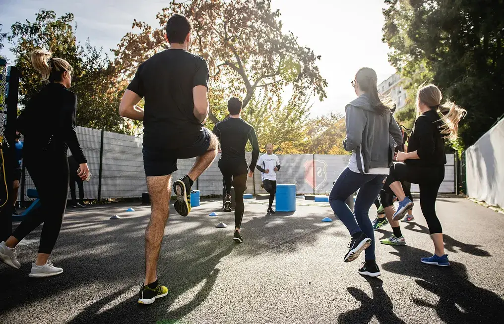 Group of people outdoors doing warm-up high knee exercises on a sunny day.