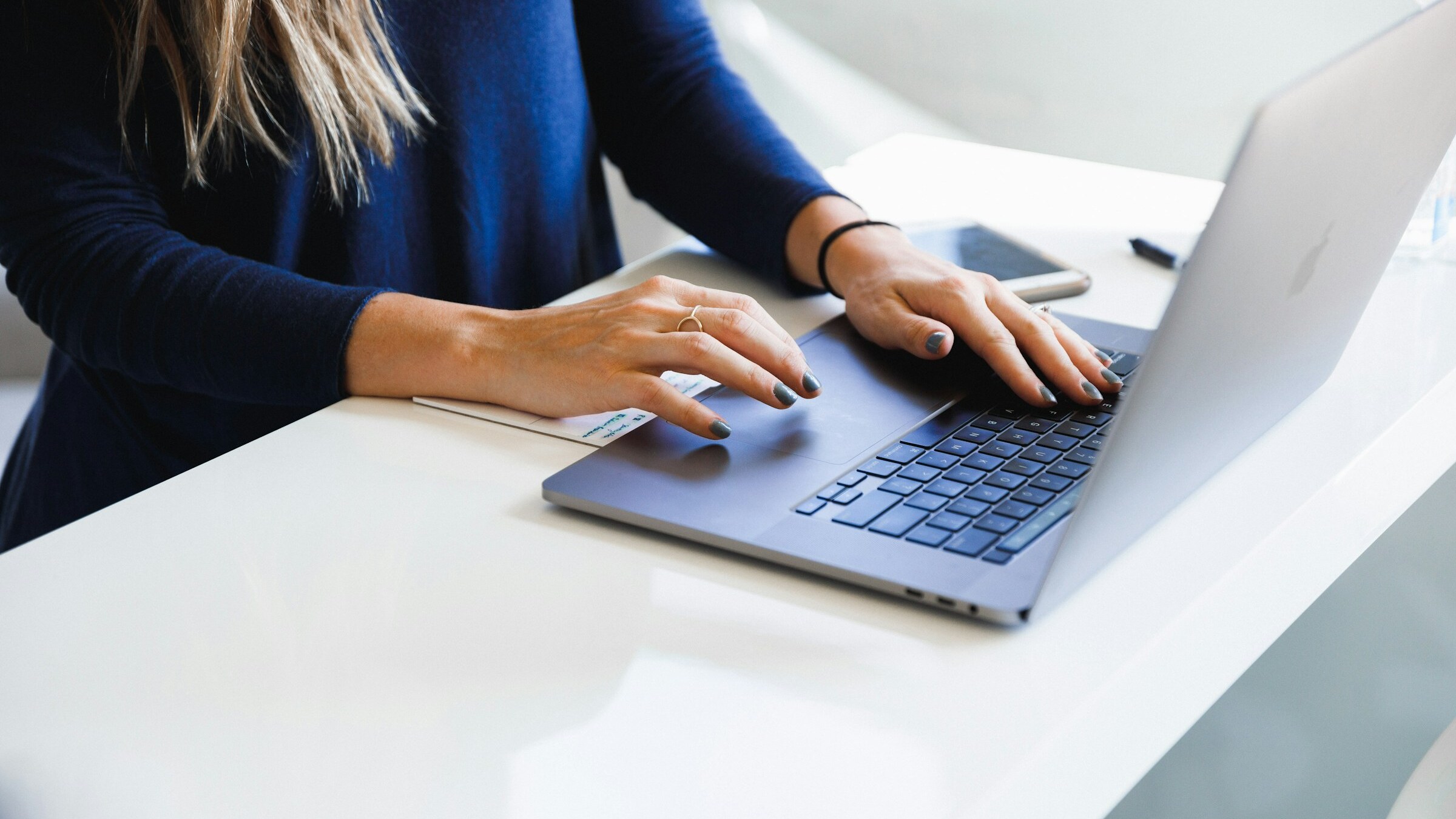 A person typing on a laptop at a white desk.