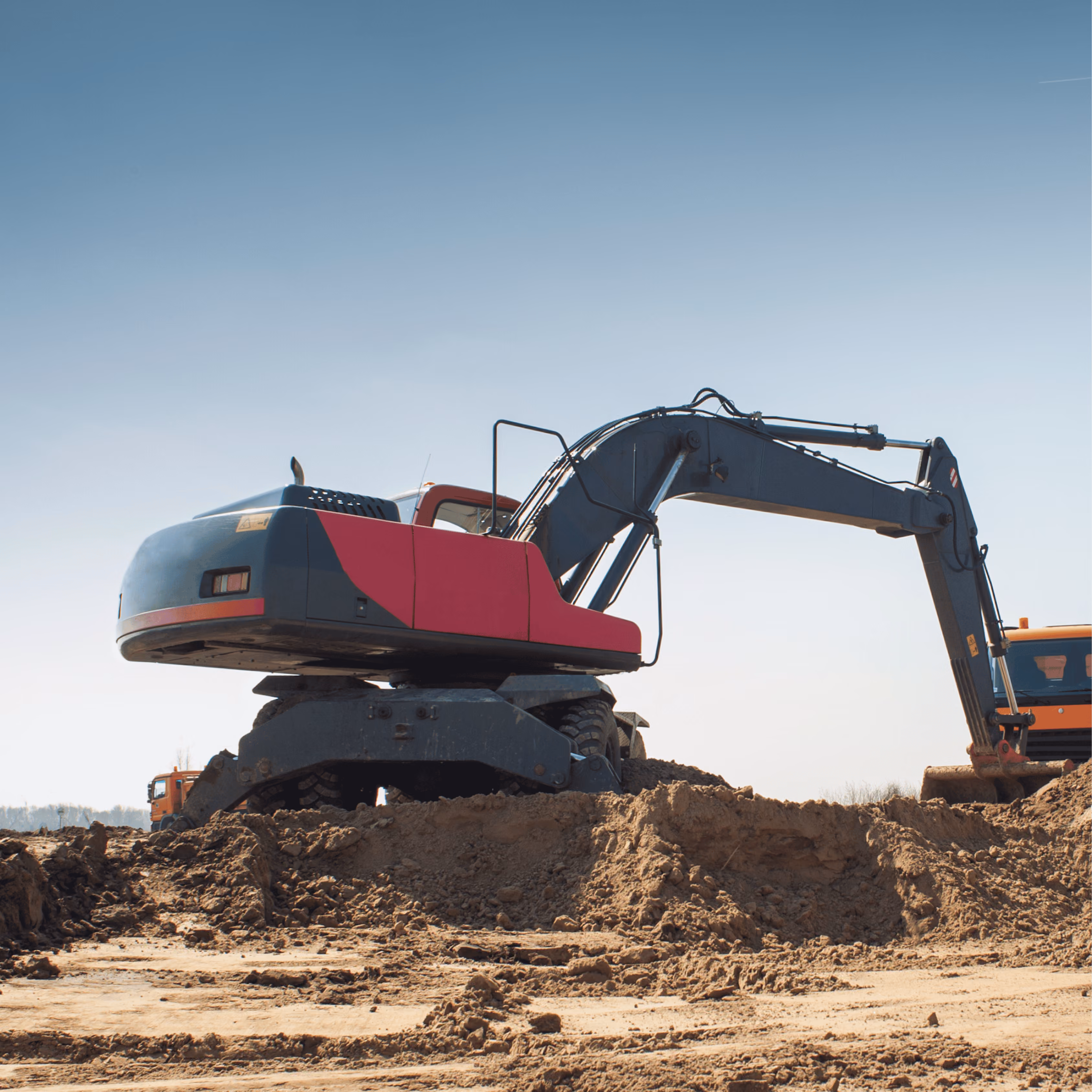 Excavator with red and gray body digging on a construction site under a clear sky.