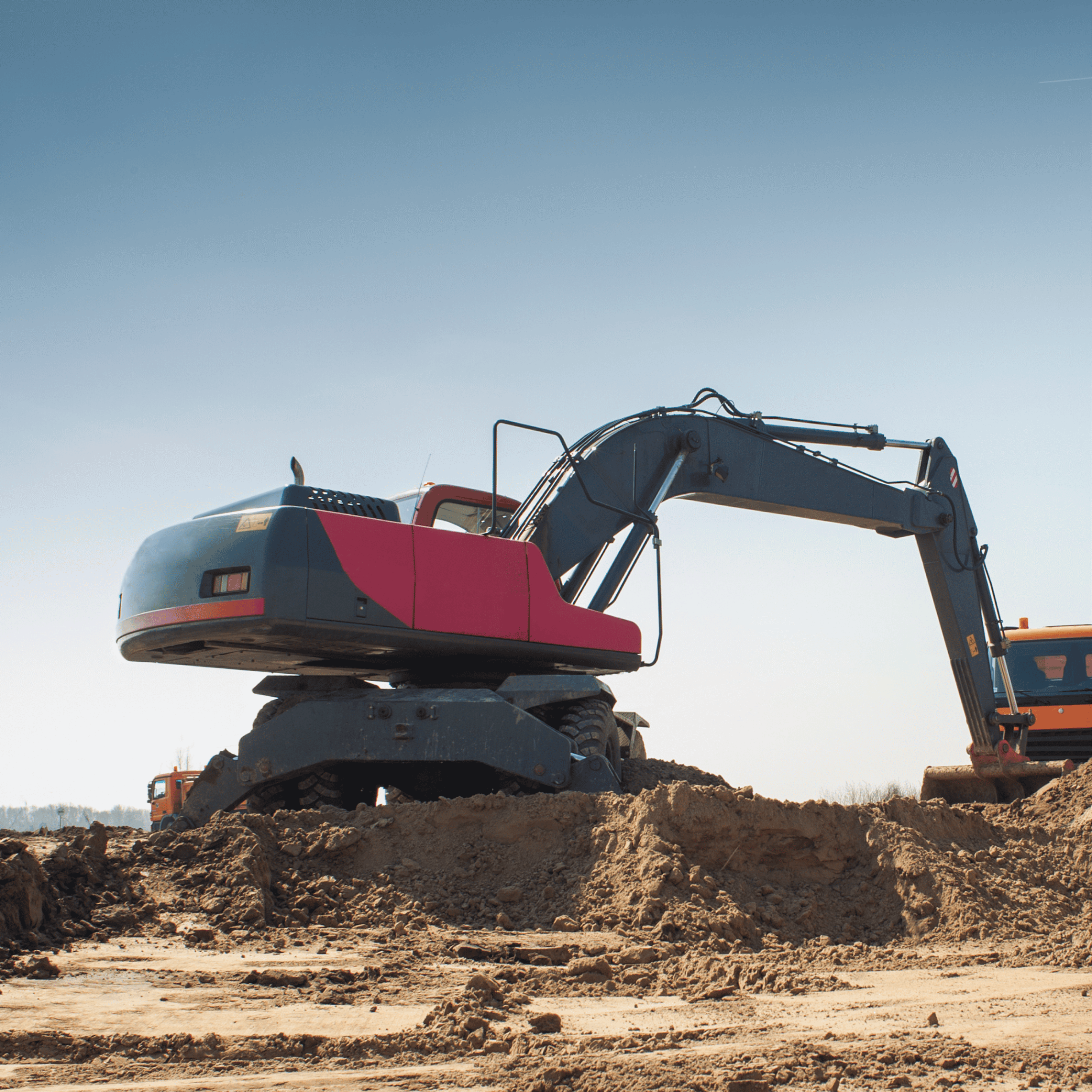 Excavator with red and gray body digging on a construction site under a clear sky.