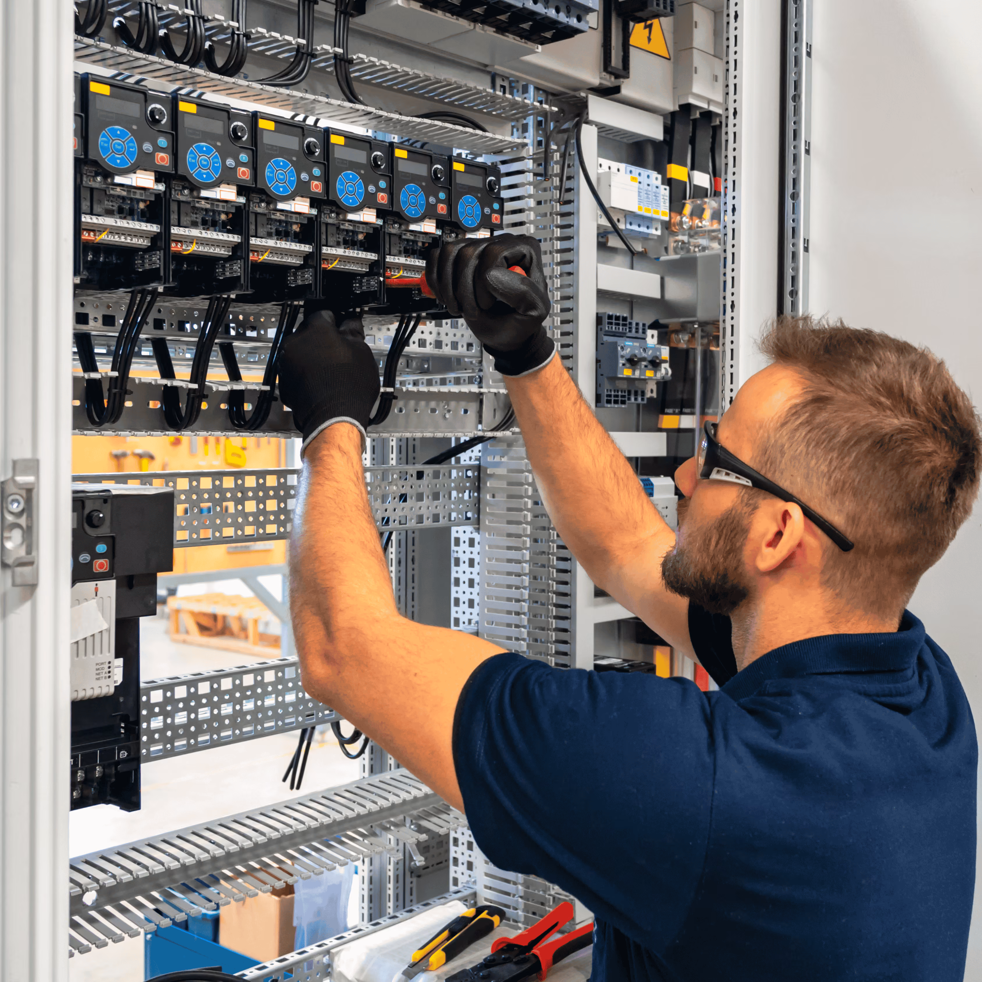 Electrician wearing gloves works on wiring inside a control panel with multiple circuit devices.