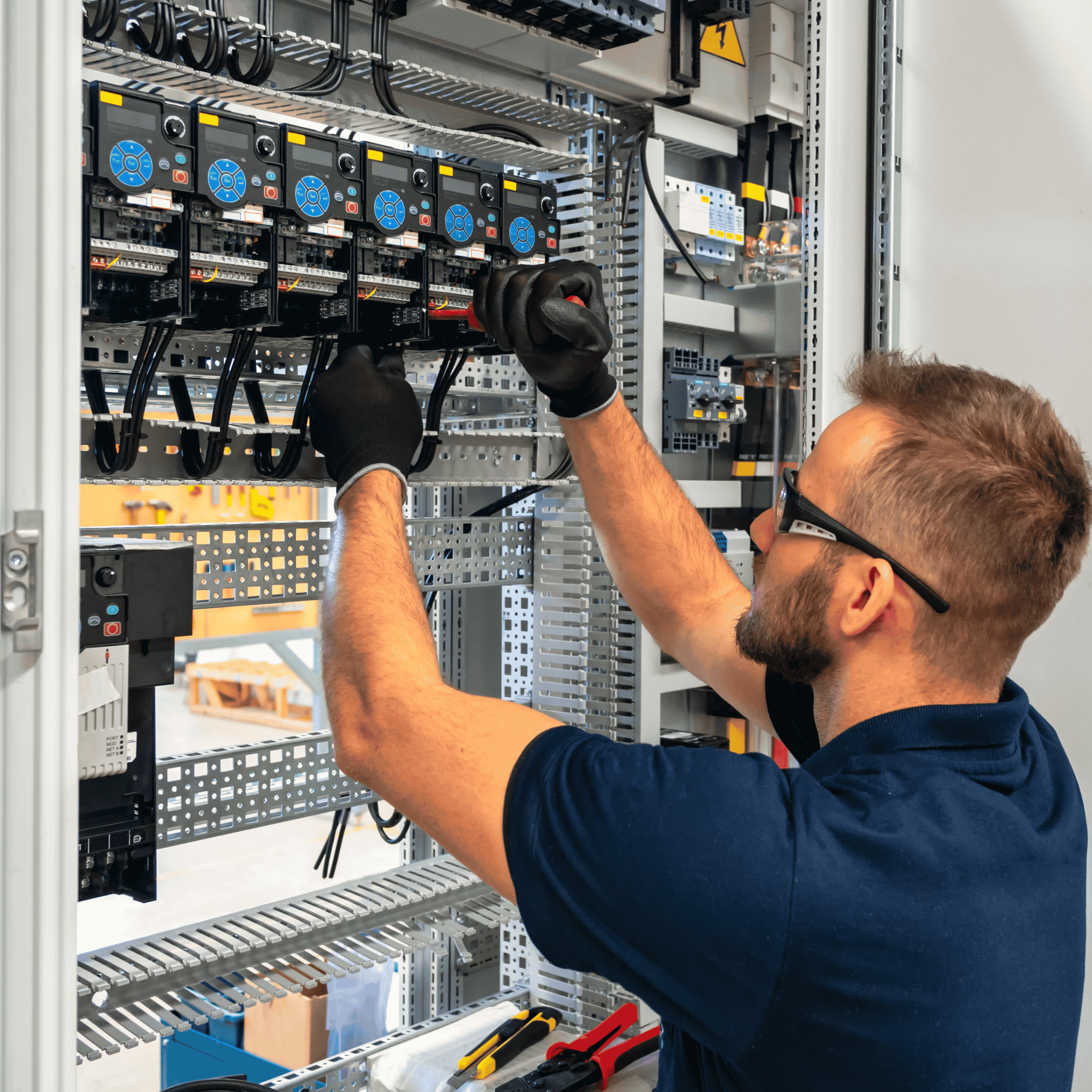 Electrician wearing gloves works on wiring inside a control panel with multiple circuit devices.