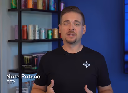 Man in black shirt speaking in front of shelves with beverage cans and a blue background.