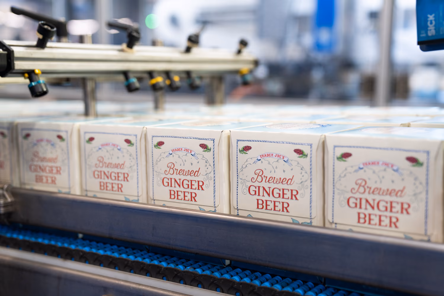 Multiple cartons of Trader Joe's Brewed Ginger Beer on a conveyor belt in a production line.