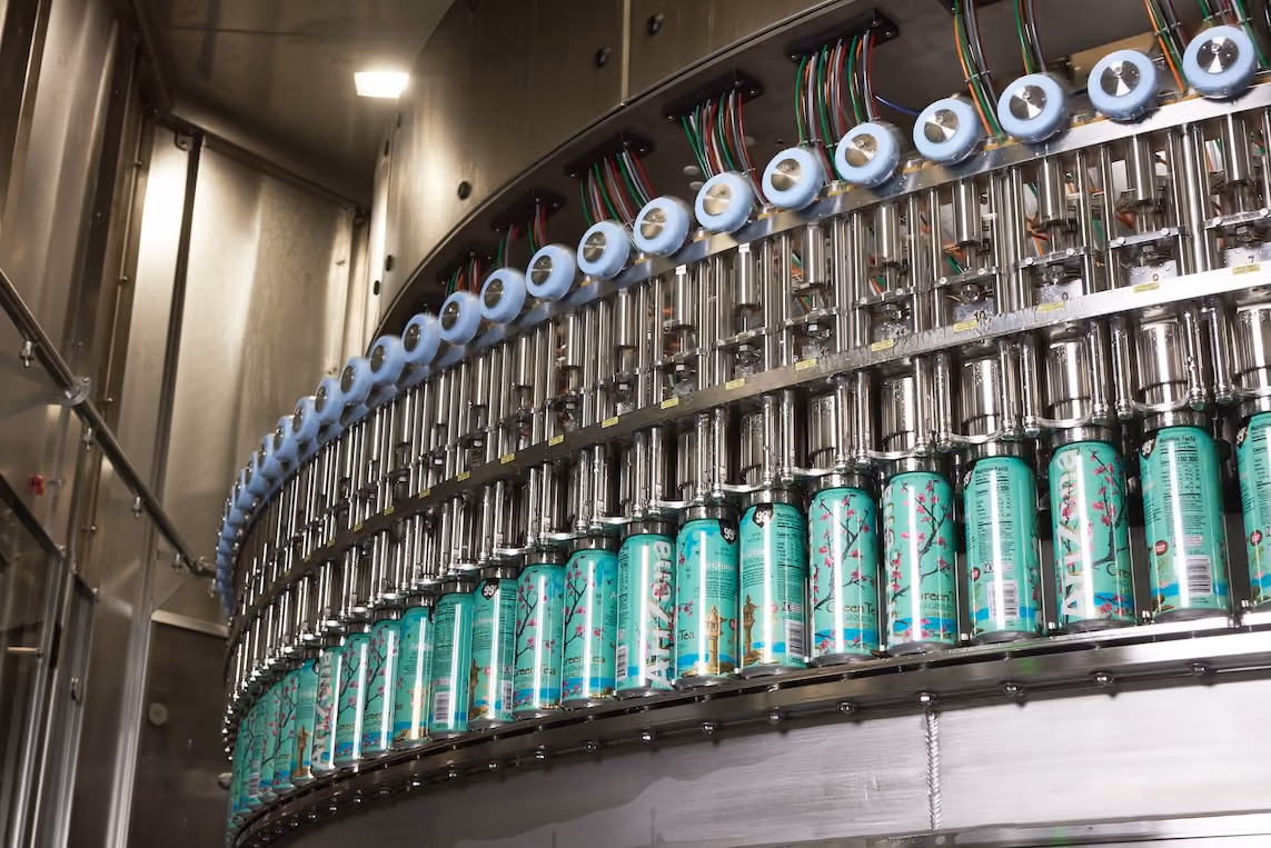 Automated machine filling tall turquoise cans of beverage in a curved production line.