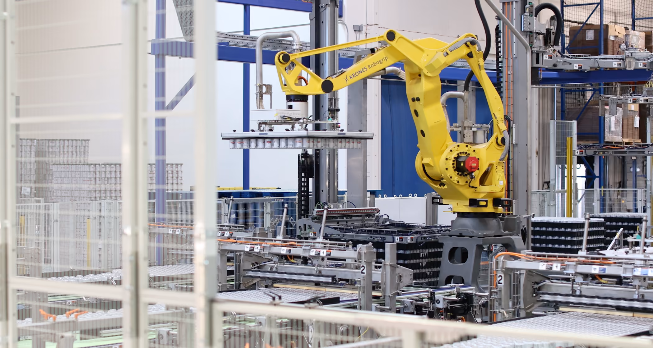 Yellow robotic arm lifting cans in an automated beverage packaging factory.