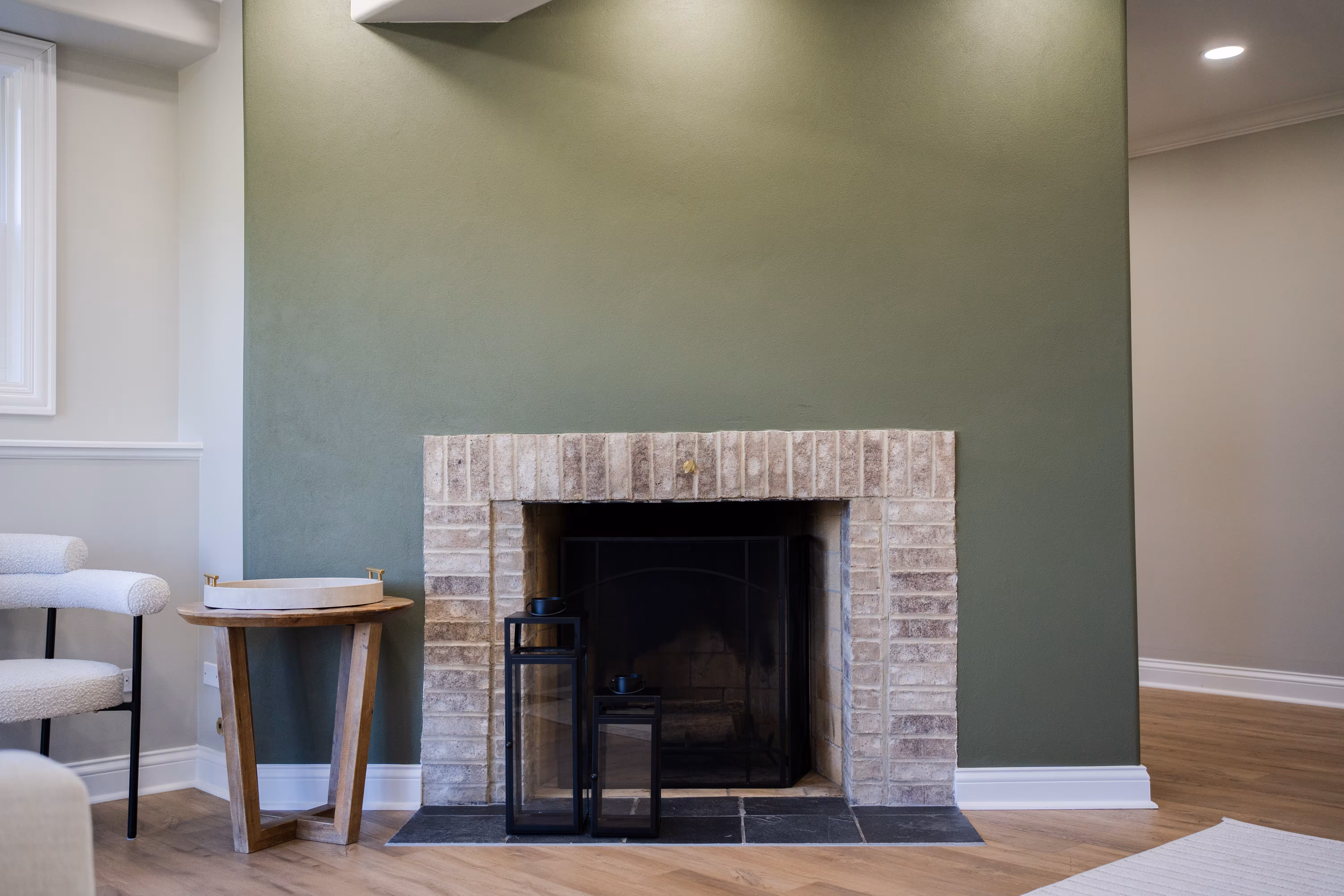 Living room with a sage green accent wall and brick fireplace, freshly painted by Metanoia Construction