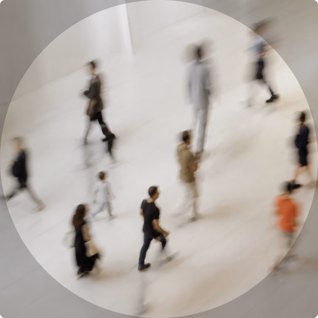 Blurred top-down view of people walking on a light-colored floor in various directions, showing motion and movement in an indoor public space.