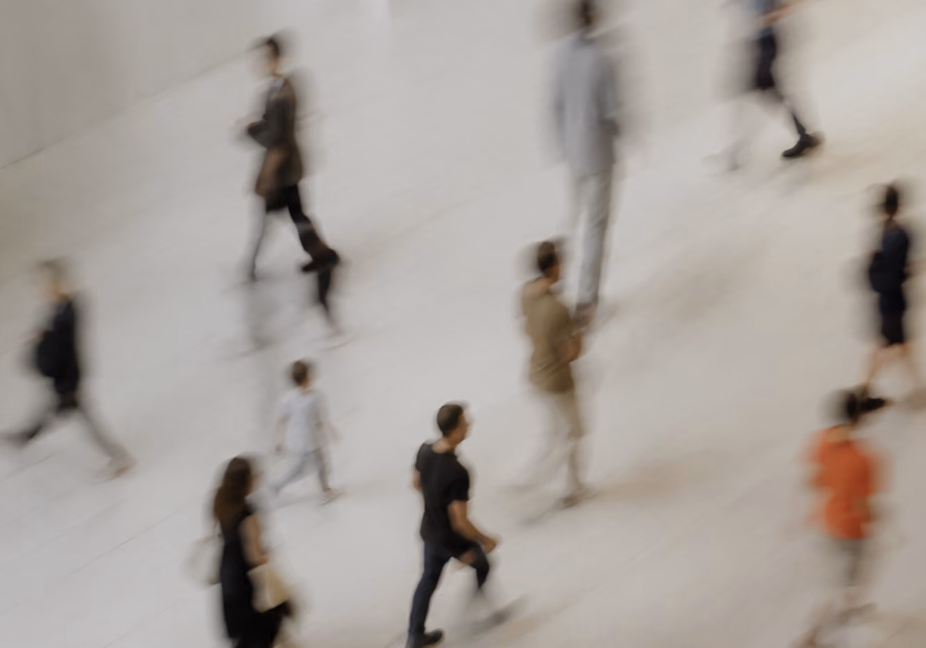 Blurred overhead view of diverse people walking in different directions on a light-colored floor, capturing motion and movement.