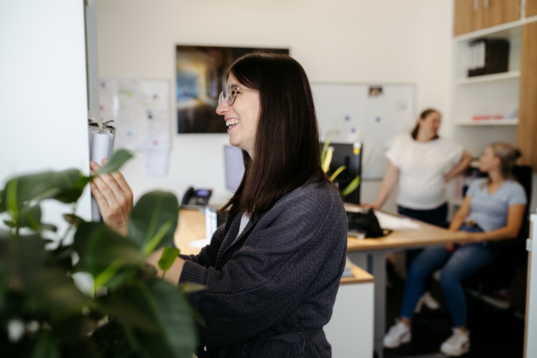 Mitarbeiterin im Büro, im Hintergrund zwei Kolleginnen am Schreibtisch