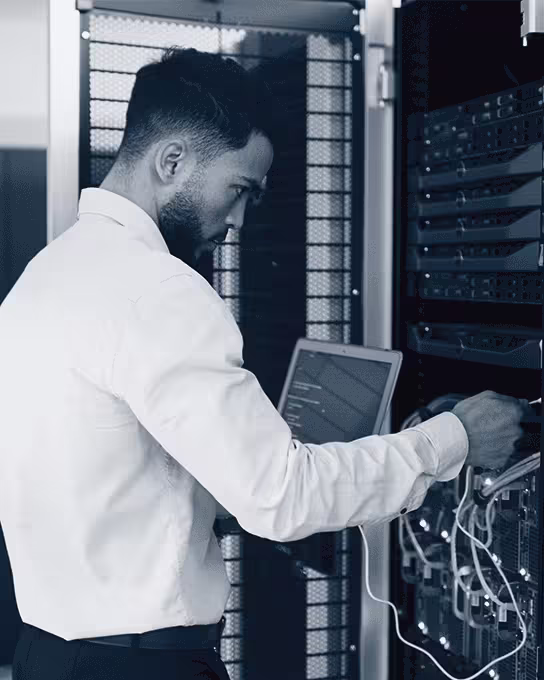 Homme en chemise blanche configure un serveur dans une salle de serveurs avec un ordinateur portable.