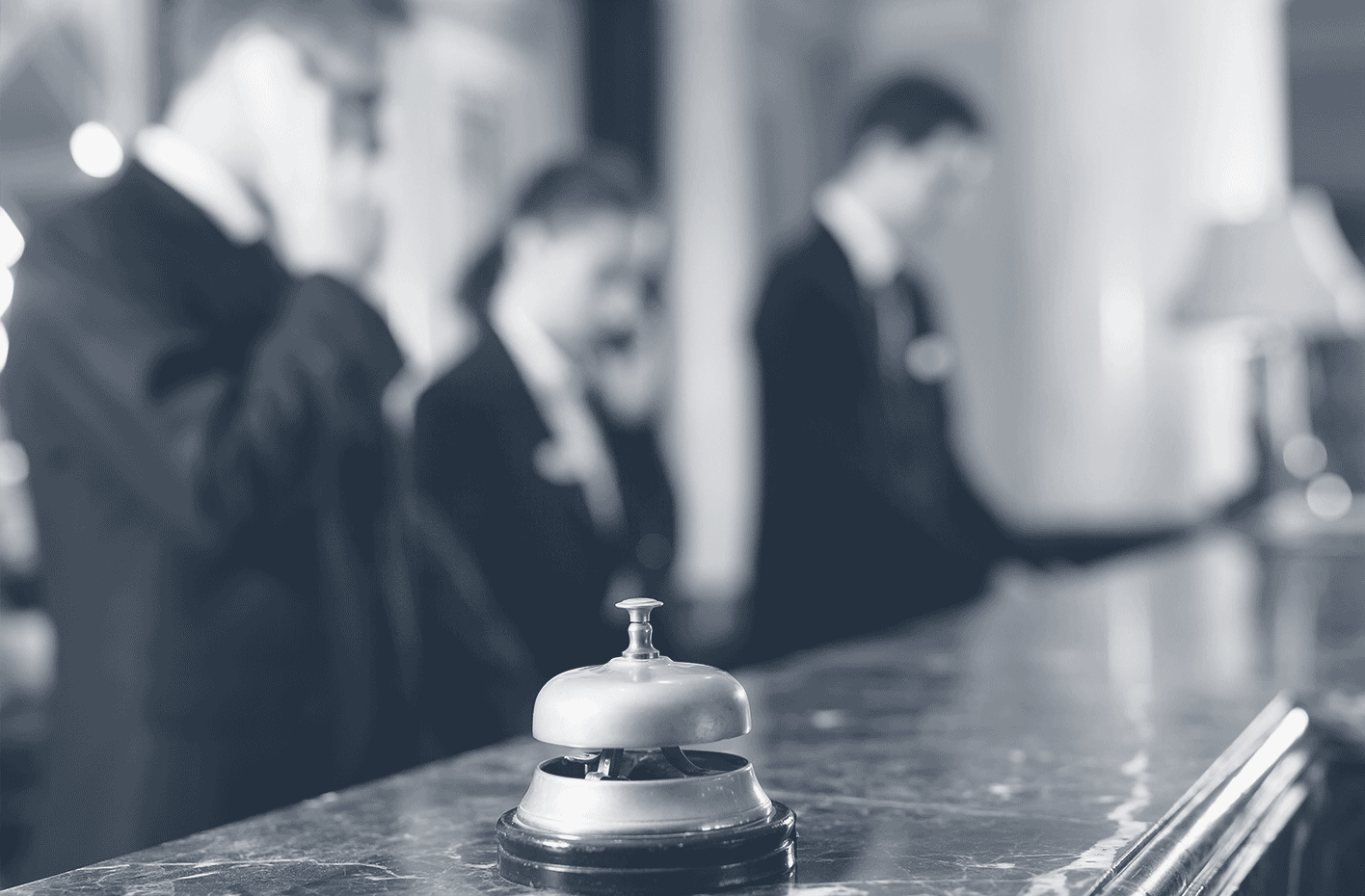 Cloche de réception d'hôtel sur comptoir en marbre avec personnel flou en arrière-plan.