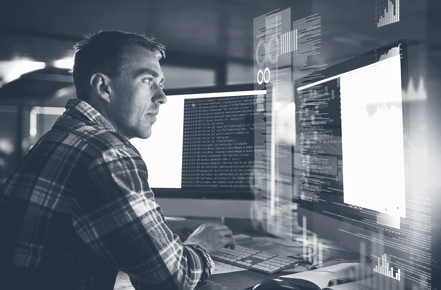 Un homme concentré travaillant sur un bureau avec deux écrans affichant des codes et données.