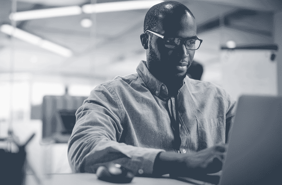 Homme portant des lunettes, concentré sur un ordinateur portable dans un bureau moderne.