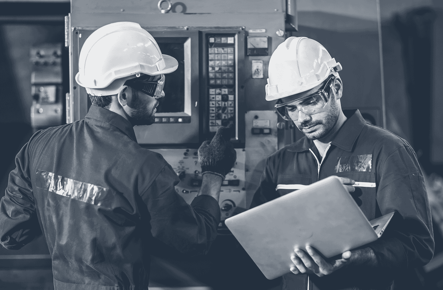 Deux ouvriers en casque de sécurité vérifient une machine industrielle, l’un utilise un ordinateur portable.