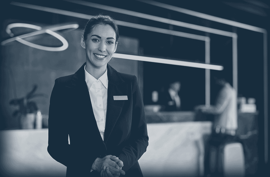 Une réceptionniste souriante dans un hall d'hôtel moderne avec deux clients au comptoir.