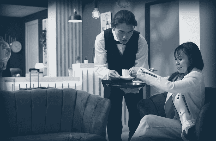 Un serveur en uniforme sert une tasse à une femme assise dans un fauteuil confortable.