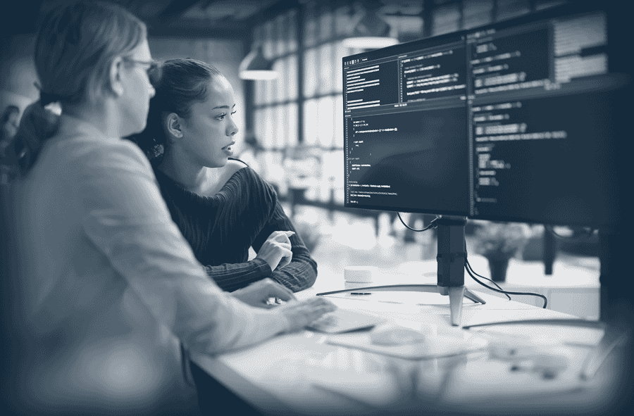 Deux femmes regardent un écran d'ordinateur montrant du code informatique dans un bureau moderne.